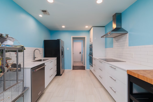 kitchen featuring tasteful backsplash, stainless steel appliances, white cabinetry, sink, and wall chimney exhaust hood