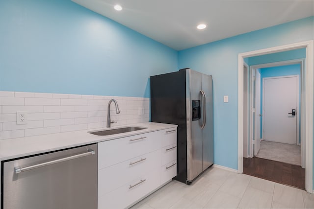 kitchen with tasteful backsplash, white cabinetry, appliances with stainless steel finishes, sink, and light hardwood / wood-style floors