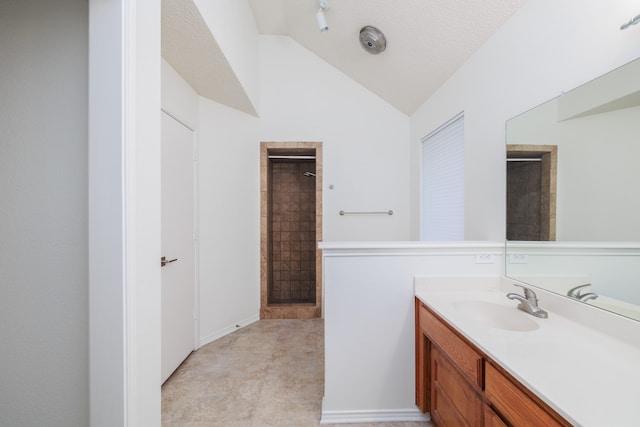 bathroom with lofted ceiling, a textured ceiling, a tile shower, and vanity