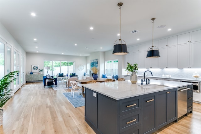 kitchen with white cabinets, hanging light fixtures, sink, and an island with sink