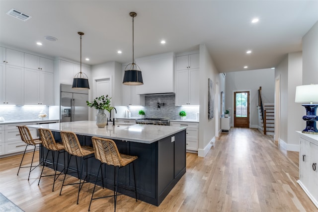 kitchen with stainless steel appliances, white cabinetry, light stone countertops, an island with sink, and light wood-type flooring