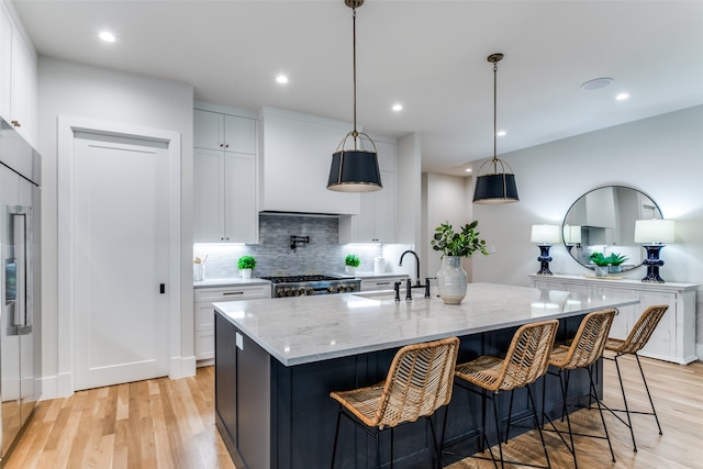 kitchen featuring white cabinetry, decorative light fixtures, sink, an island with sink, and light hardwood / wood-style flooring