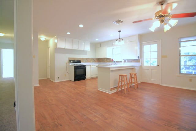 kitchen featuring white cabinets, kitchen peninsula, a kitchen breakfast bar, black range, and light hardwood / wood-style flooring