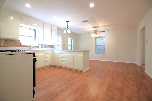 kitchen with kitchen peninsula, range, tasteful backsplash, light wood-type flooring, and decorative light fixtures