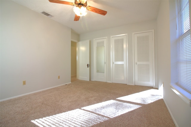 unfurnished bedroom featuring light colored carpet, ceiling fan, and two closets