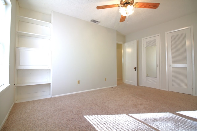 unfurnished bedroom with a textured ceiling, light carpet, ceiling fan, and two closets