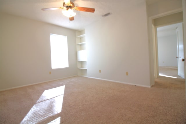 empty room featuring built in shelves, ceiling fan, and carpet floors