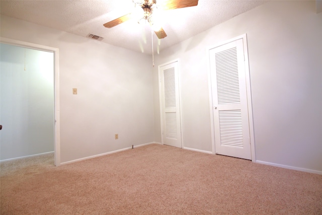 unfurnished bedroom featuring ceiling fan, a textured ceiling, light carpet, and two closets