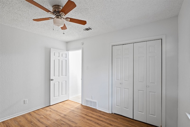 unfurnished bedroom with a textured ceiling, wood-type flooring, ceiling fan, and a closet