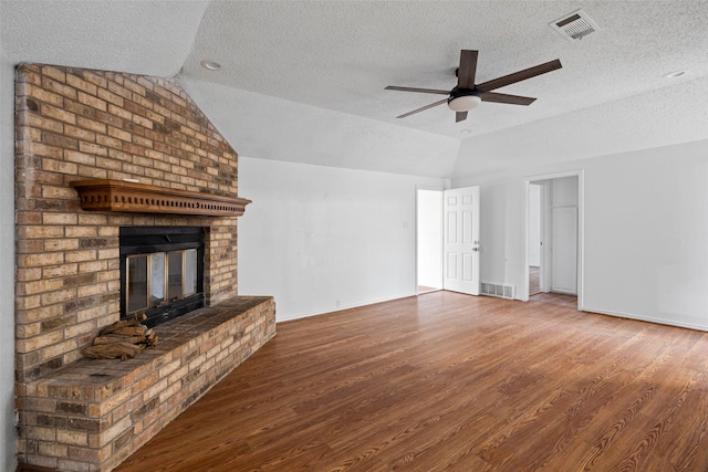 unfurnished living room with a brick fireplace, wood-type flooring, vaulted ceiling, a textured ceiling, and ceiling fan