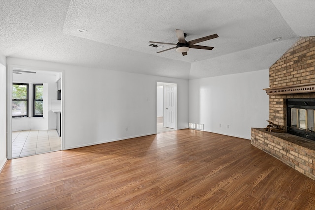 unfurnished living room featuring a brick fireplace, wood-type flooring, a textured ceiling, and ceiling fan