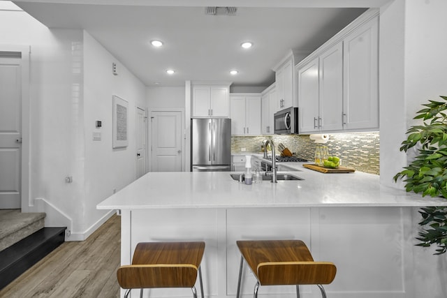 kitchen with stainless steel appliances, light hardwood / wood-style floors, kitchen peninsula, a breakfast bar area, and white cabinets