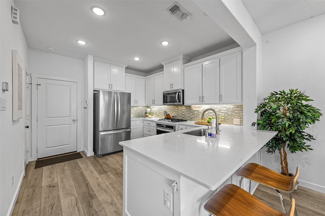 kitchen featuring light hardwood / wood-style flooring, sink, a kitchen breakfast bar, white cabinetry, and appliances with stainless steel finishes