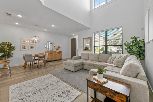 living room featuring a towering ceiling, light hardwood / wood-style flooring, and an inviting chandelier