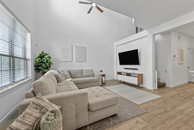 living room featuring ceiling fan, a high ceiling, and wood-type flooring