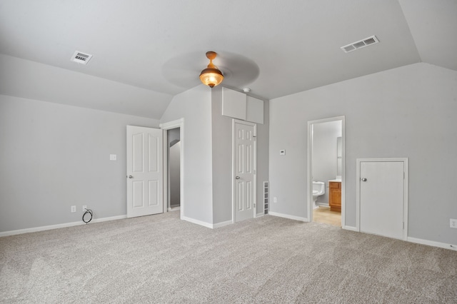 interior space featuring ceiling fan, ensuite bath, vaulted ceiling, and light colored carpet