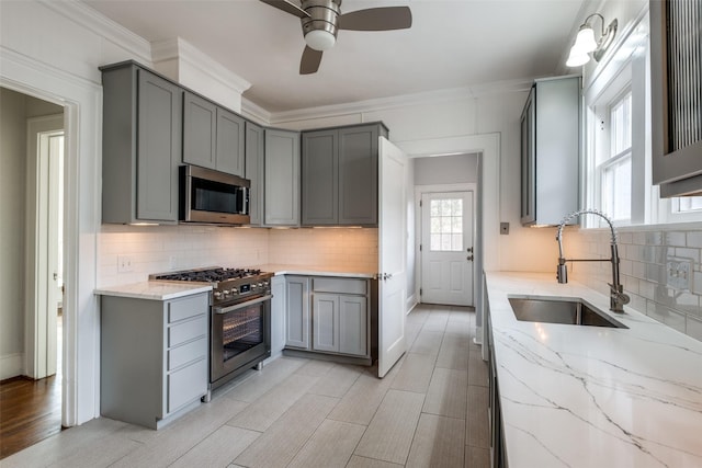 kitchen featuring a sink, appliances with stainless steel finishes, gray cabinets, and light stone counters