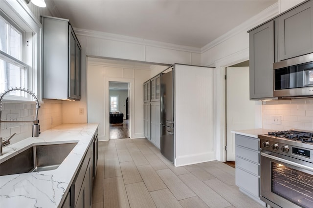 kitchen featuring stainless steel appliances, a sink, ornamental molding, gray cabinets, and light stone countertops