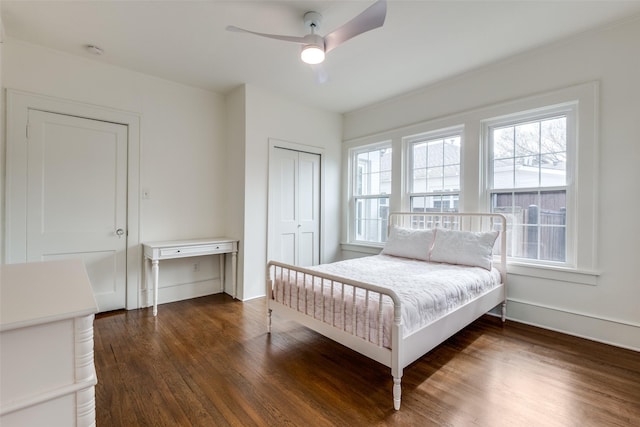 bedroom with dark wood-type flooring, a closet, a ceiling fan, and baseboards