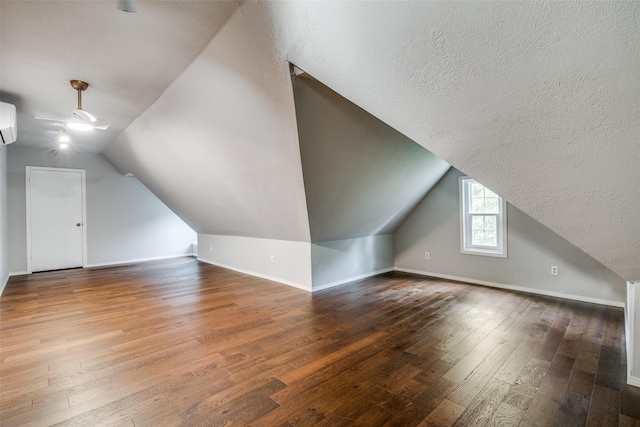 additional living space with lofted ceiling, an AC wall unit, hardwood / wood-style floors, and baseboards