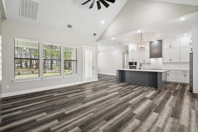 kitchen featuring white cabinetry, a center island with sink, ceiling fan with notable chandelier, high vaulted ceiling, and dark hardwood / wood-style flooring