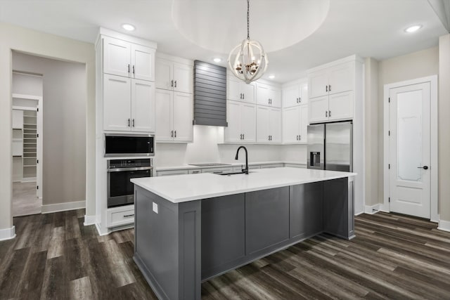 kitchen featuring white cabinetry, appliances with stainless steel finishes, decorative light fixtures, and an island with sink