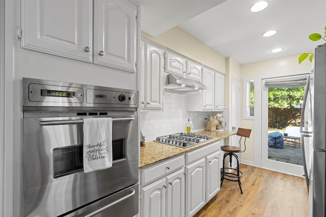 kitchen featuring stainless steel appliances, light stone counters, tasteful backsplash, white cabinets, and light wood-type flooring