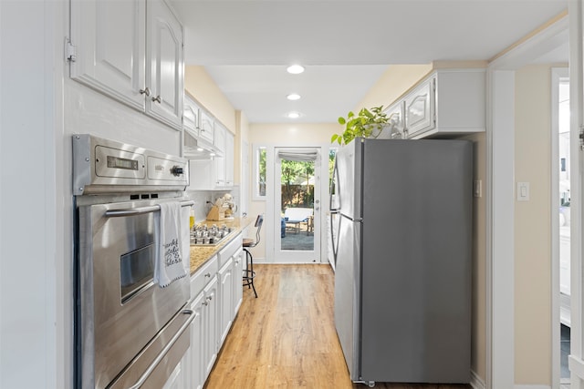 kitchen featuring light stone counters, light wood-type flooring, appliances with stainless steel finishes, decorative backsplash, and white cabinets