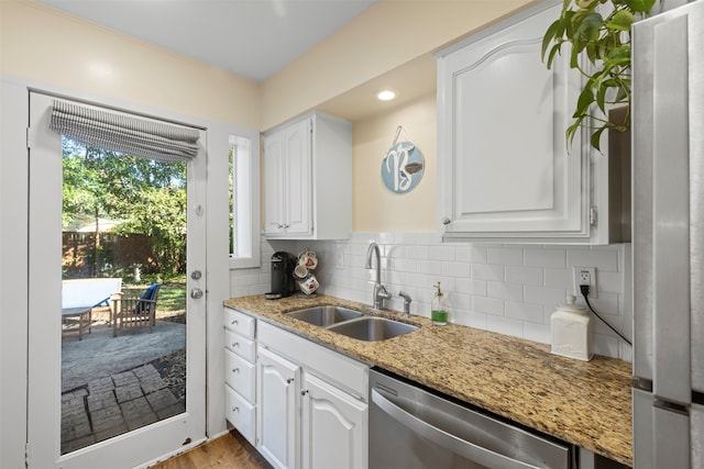 kitchen with stainless steel dishwasher, sink, light stone countertops, and white cabinets