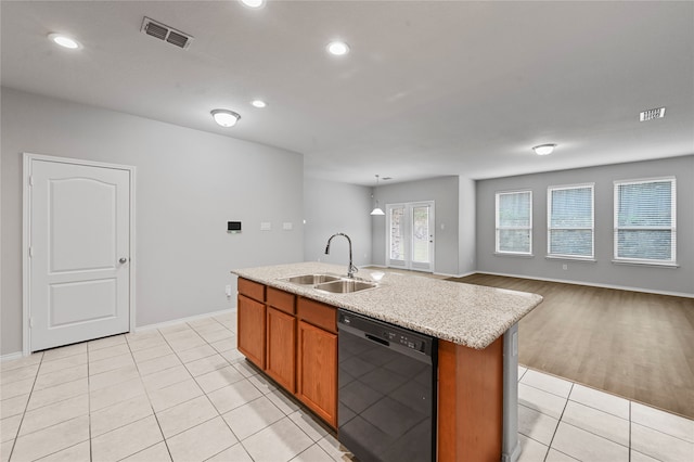 kitchen featuring light hardwood / wood-style floors, a center island with sink, black dishwasher, hanging light fixtures, and sink