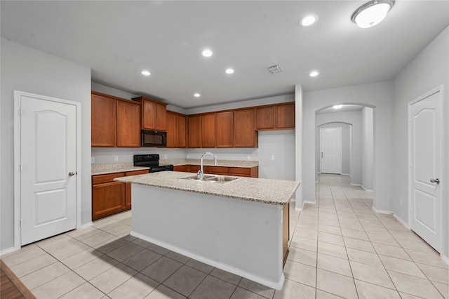 kitchen with black appliances, sink, an island with sink, light tile patterned flooring, and light stone countertops