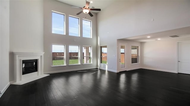 unfurnished living room featuring a towering ceiling, a wealth of natural light, dark hardwood / wood-style floors, and ceiling fan