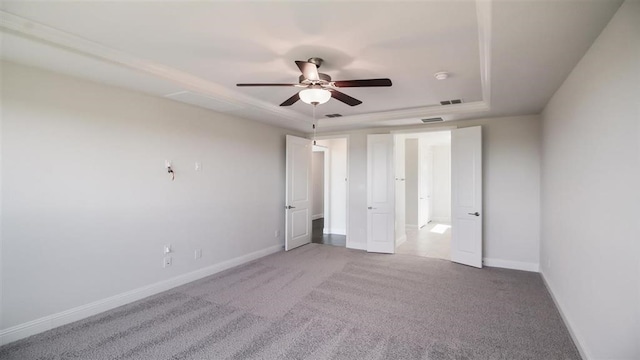 empty room featuring a tray ceiling, carpet flooring, and ceiling fan