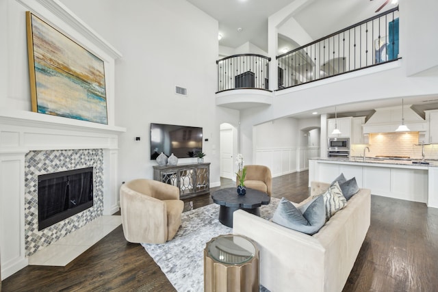 living room with a fireplace, a towering ceiling, and dark wood-type flooring