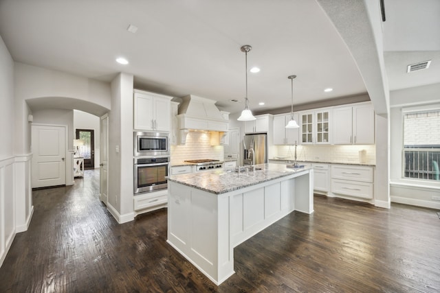 kitchen featuring a center island with sink, white cabinets, stainless steel appliances, and custom range hood