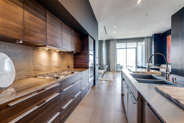 kitchen with tasteful backsplash, appliances with stainless steel finishes, dark brown cabinetry, light tile patterned floors, and sink