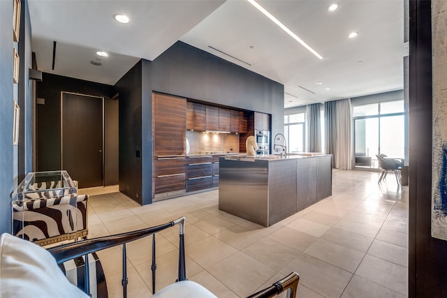 kitchen featuring dark brown cabinets, a center island with sink, and light tile patterned floors