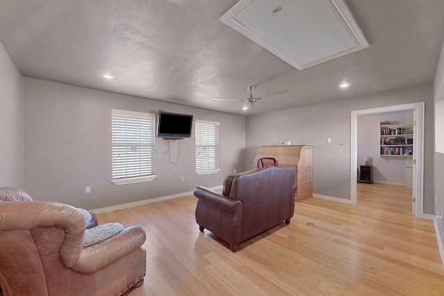 living room with ceiling fan, a textured ceiling, and light hardwood / wood-style floors