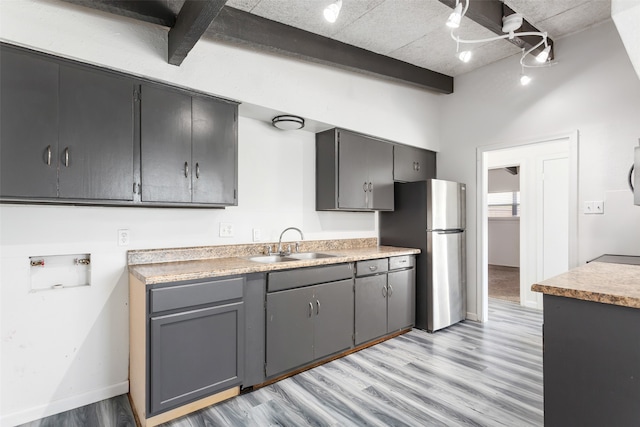 kitchen with gray cabinetry, light wood-type flooring, stainless steel refrigerator, sink, and beamed ceiling