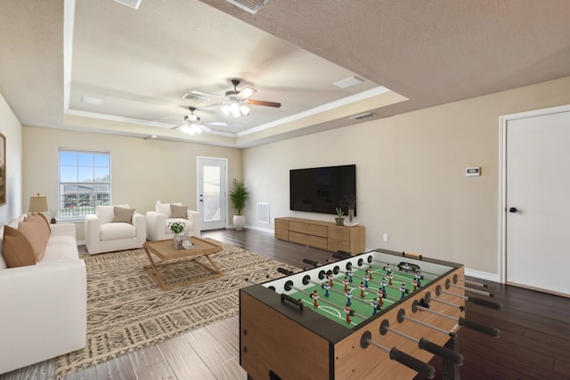 rec room with dark wood-type flooring, a tray ceiling, a textured ceiling, and ceiling fan