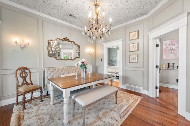 dining space with hardwood / wood-style flooring, an inviting chandelier, and ornamental molding