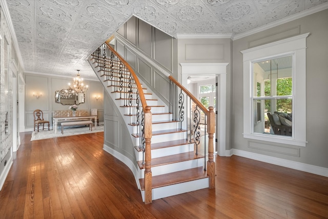 stairway with wood-type flooring, an inviting chandelier, and crown molding