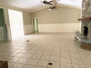 unfurnished living room with a stone fireplace, vaulted ceiling, light tile patterned floors, ceiling fan, and crown molding