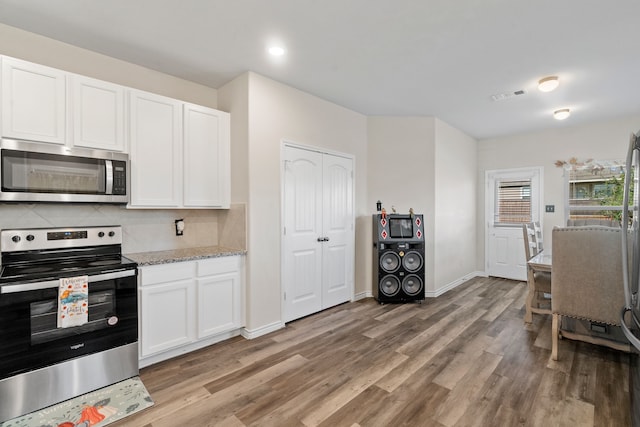 kitchen with appliances with stainless steel finishes, light stone countertops, backsplash, white cabinets, and light wood-type flooring