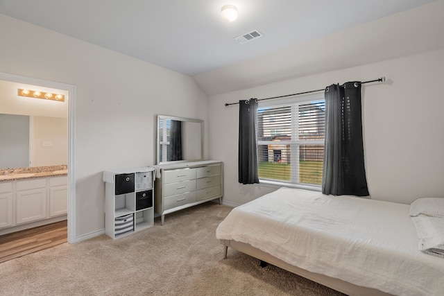 bedroom with ensuite bath, light carpet, and vaulted ceiling