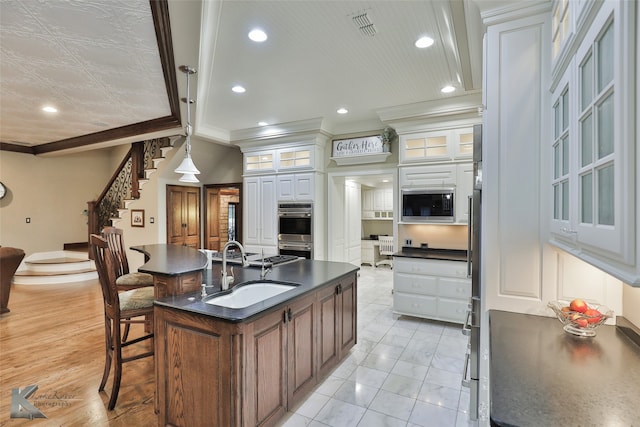 kitchen featuring white cabinets, a center island with sink, sink, and crown molding