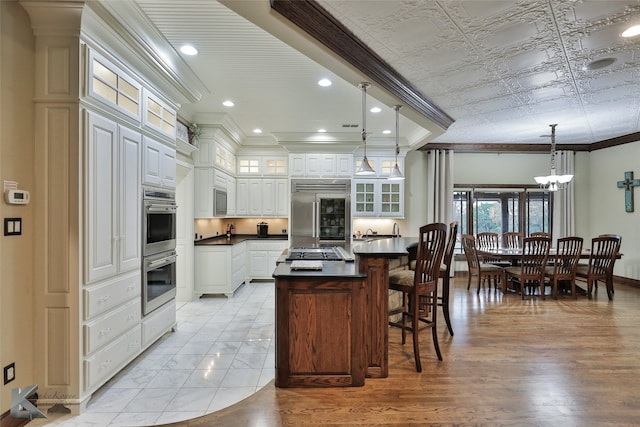 kitchen featuring crown molding, built in appliances, pendant lighting, light hardwood / wood-style floors, and white cabinets