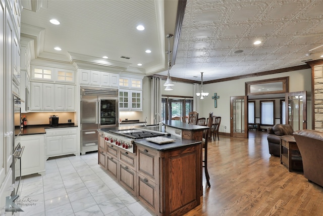 kitchen with crown molding, light wood-type flooring, appliances with stainless steel finishes, an island with sink, and white cabinets