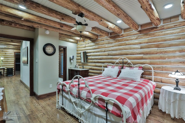 bedroom featuring beam ceiling, hardwood / wood-style flooring, ceiling fan, and log walls