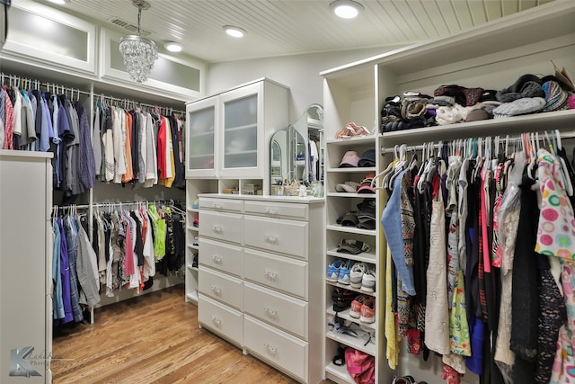 spacious closet featuring light hardwood / wood-style flooring, a chandelier, and vaulted ceiling